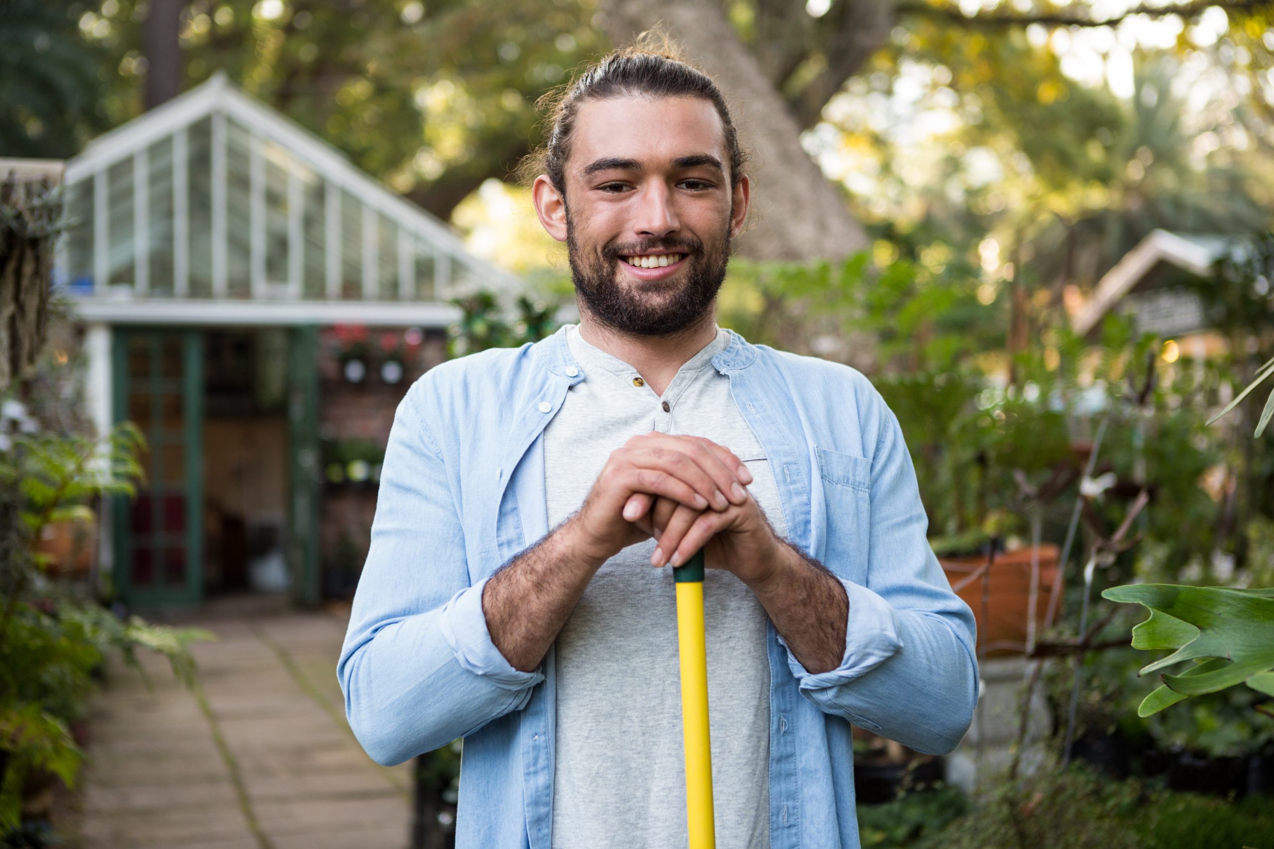 Portrait of happy young male gardener with work tool at garden;