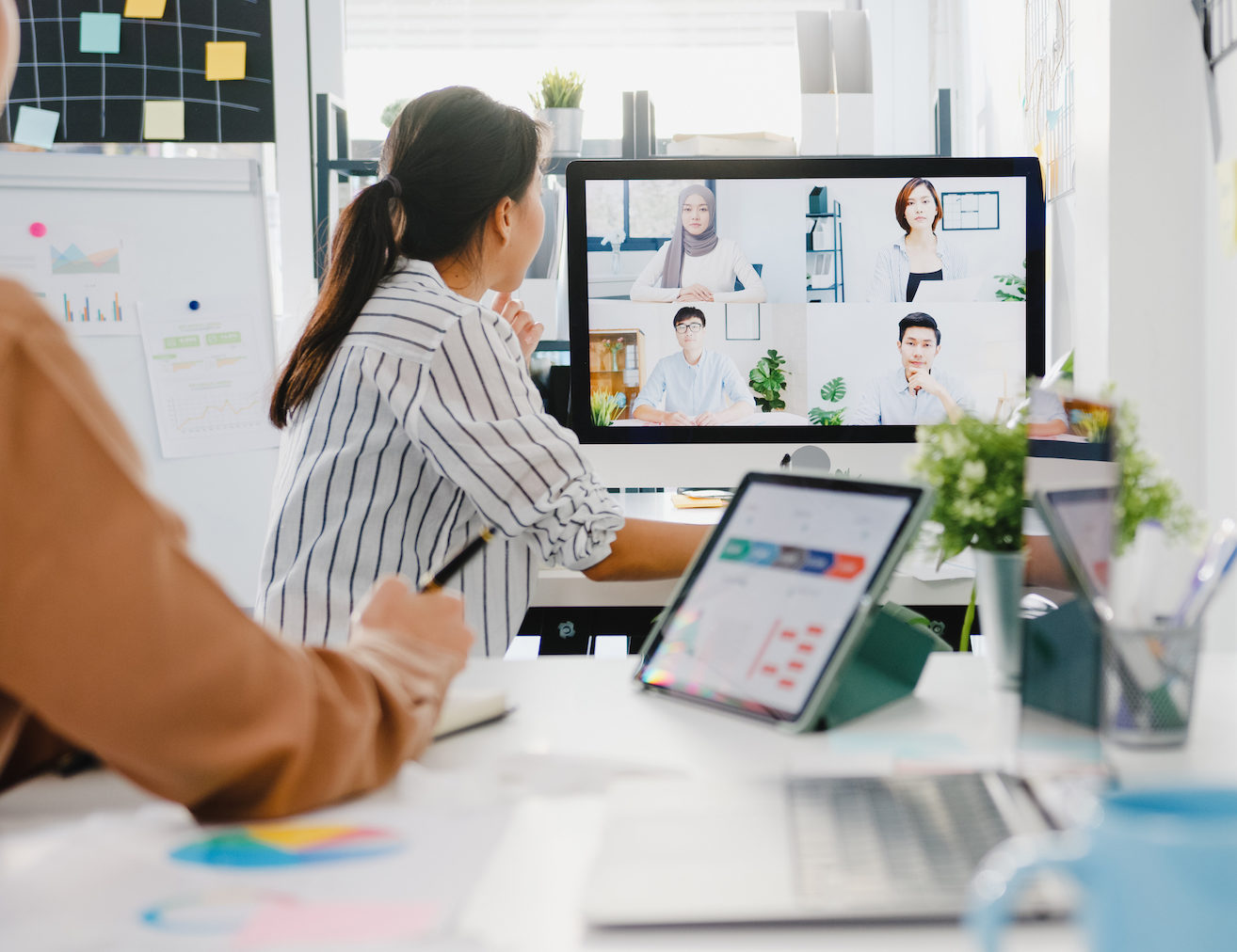 Asia businesspeople using desktop talk to colleagues discussing business brainstorm about plan in video call meeting in new normal office. Lifestyle social distancing and work after corona virus.;