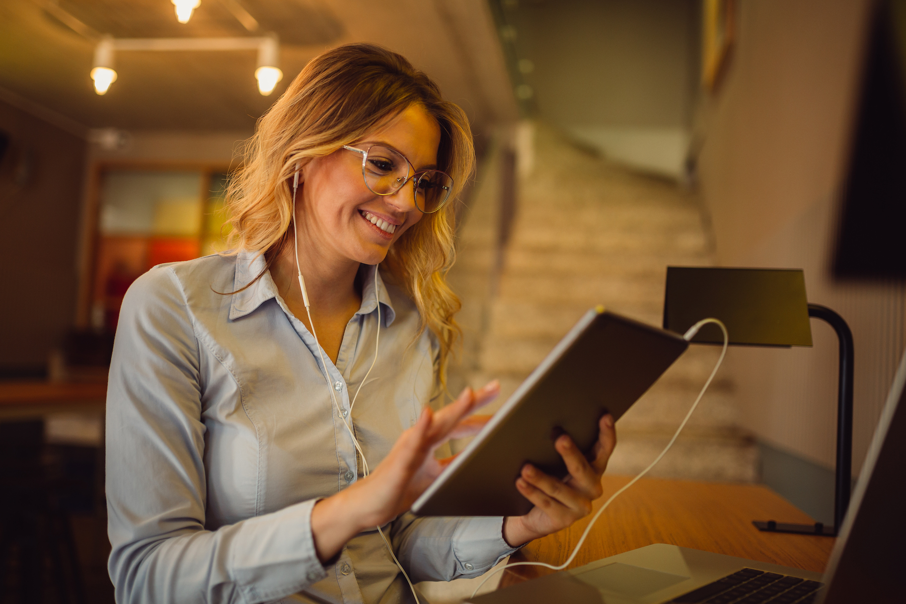 Charming young business woman using tablet computer and earphones to attend online meeting